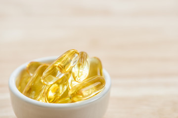 Cod liver oil omega 3 gel capsules in bowl on floor wood.