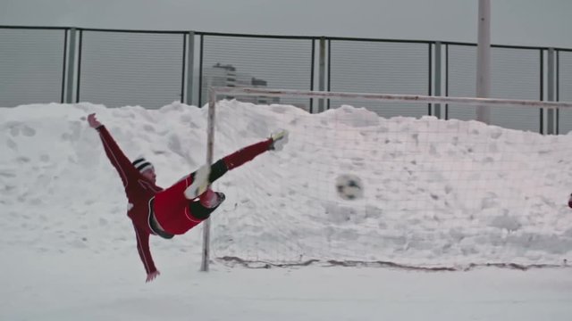 Slow motion of skillful teenage soccer player in red uniform performing bicycle kick shot and scoring own goal during winter match at snow-covered outdoor stadium