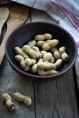 Some peanuts in a cyan bowl on a wooden table.