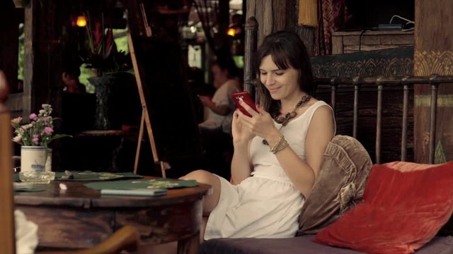 Young, pretty woman using smartphone sitting on sofa in cafe 

