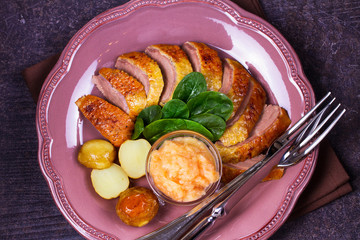Spiced slow roast duck, apple sauce, spinach and potato, served on pink plate. View from above, top studio shot