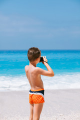 Beach vacation dream. Handsome young boy enjoying in beautiful tropical beach and taking some photos with his camera.