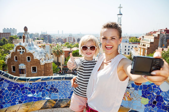 Smiling mother and baby taking selfie with camera at Park Guell