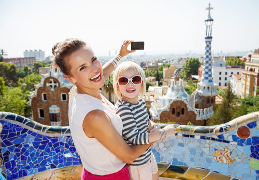 Smiling mother and baby taking photos with camera at Park Guell