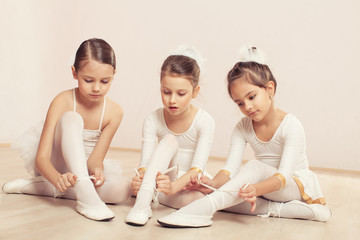 Fototapeta premium Little ballerinas sitting on the floor and adjusting slippers 