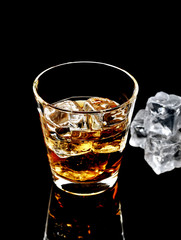 Whiskey with ice in glass isolated on black background 
