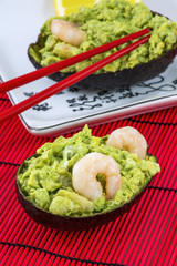 Green avocado salad with shrimps, lemon and red chopsticks lies on the white plate on the red background