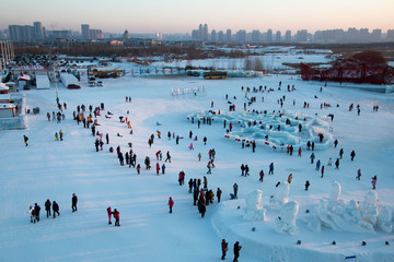 Masses of people sledding in Harbin as the sun sets behind them.