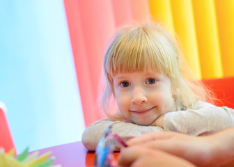 Fototapeta premium Grinning little girl resting head on arms at table