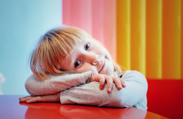Fototapeta premium Grinning little girl resting head on arms at table
