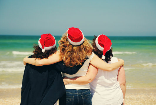 Three beautiful women wearing christmas hat walking on the seasi