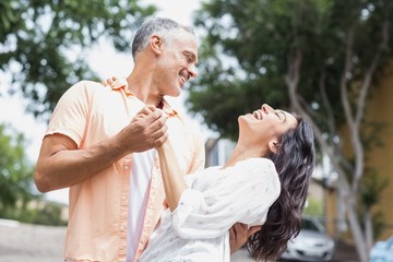 Cheerful couple dancing against trees in city