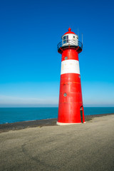 Red and white lighthouse against a bright blue sky