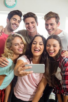 Happy friends smiling while taking selfie at home