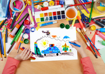 Fototapeta premium child drawing police car and helicopter, top view hands with pencil painting picture on paper, artwork workplace