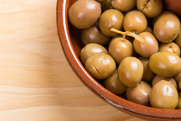 Green olives and seeds on brown ceramic plate.From above