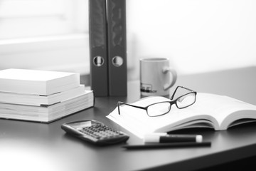 Schreibtisch / Arbeitsplatz mit Büchern, Brille, Taschenrechner und Ordnern, schwarz weiß