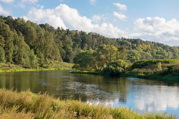 Wide river in green banks overgrown with woods