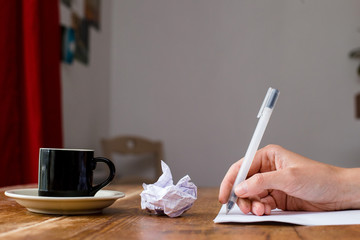 Hand holding and writing a pen. Coffee at a wooden table. Selective focus.