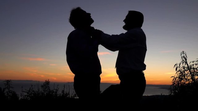 Silhouette of two businessmen fighting during sunset, super slow motion
