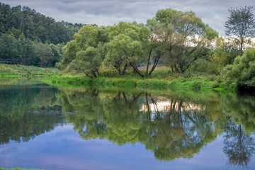 Wide river in green banks overgrown with woods