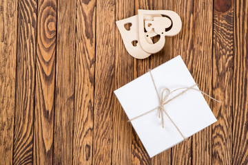 White gift box on a wooden background with decorative hearts