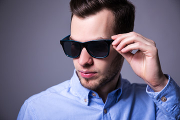 close up portrait of young handsome man in sunglasses over gray