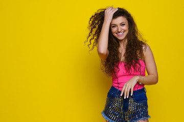 Young and beautiful curly girl in a pink shirt and blue shorts on a yellow background