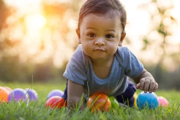 Fototapeten Cute asian baby crawling in the green grass and colorful ball © pkproject