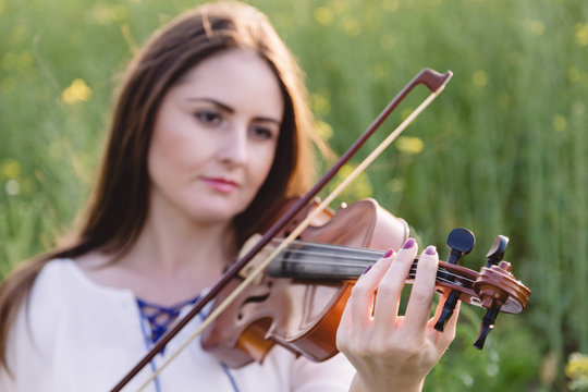 Young woman playing violin in a green field. Focus on the han