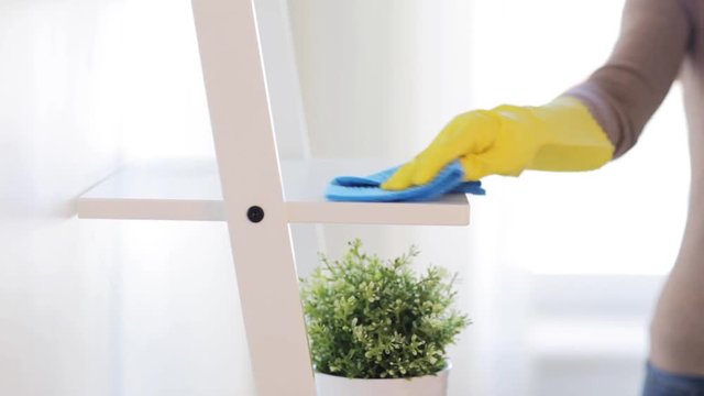 woman with duster cleaning shelf from dust at home