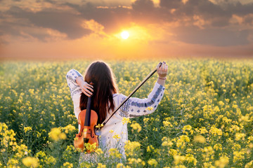 Young woman playing violin in a field at sunset