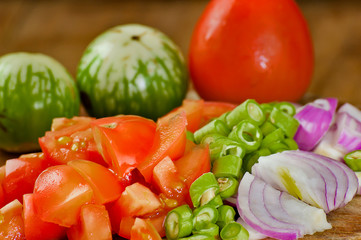 Eggplant, beans, tomatoes, onions on a cutting board.