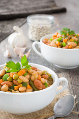White beans with vegetables in a bowl on wood