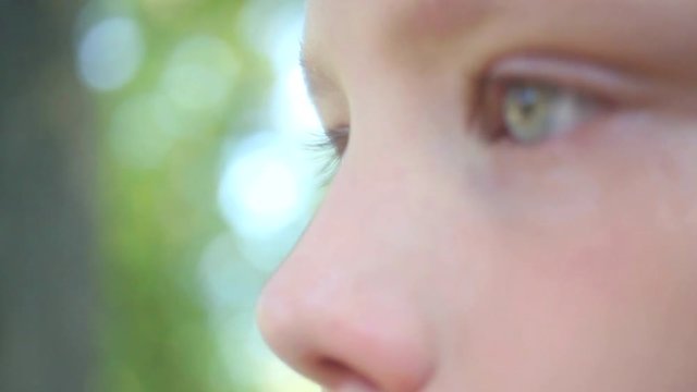 Macro of beautiful sad grey eyes of little kid after crying. Close up of unhappy children face wet from tears isolated at green trees leaves background. Real time video