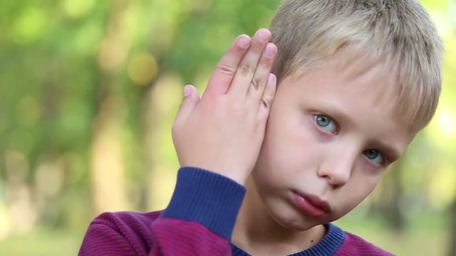 Closeup of face of adorable sad child after being stinged by bee on finger. Portrait of small boy showing his aching hand outside. Children face wet from tears in green summer park. Real time video.
