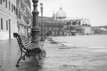 Langzeitbelichtung einer typischen Holzbank an der Promenade in Venedig (Venezia) an einem regnerischen Tag im Herbst ohne Menschen, Italien, Europa, Schwarzweiß