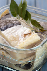 salted cod fish in water in glass dish on blue wooden background