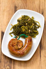 traditional portuguese smoked sausage with turnip greens on white plate on brown wooden  background