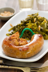 traditional portuguese smoked sausage with turnip greens on white plate on brown background