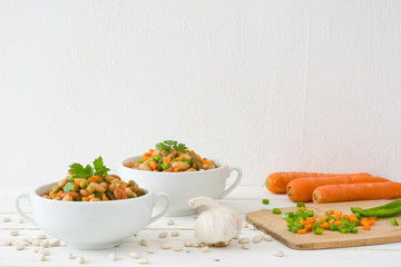 White beans with vegetables on white wood
