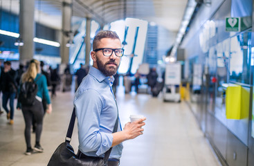 Hipster businessman holding a coffee cup, subway station