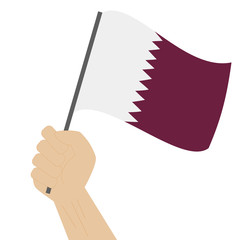 Hand holding and raising the national flag of Qatar