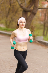 Young athletic woman jogging with dumbbells in park
