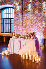 Table set for banquet in loft. Vintage room with brick walls without plaster or wallpapers. Table decorated with candles, fabric and flowers.