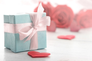Obraz na płótnie Canvas Gift box, rose flowers and decorative hearts on light wooden background