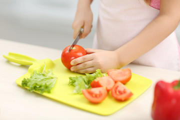 Little girl's  hands cutting vegetables on a board.