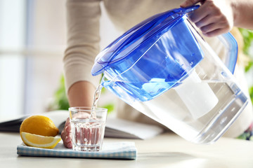 Woman pouring water from filter jug into glass in the kitchen - obrazy, fototapety, plakaty