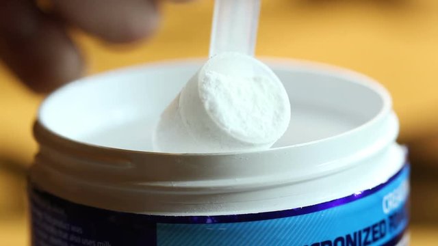 Taking a scoop of creatine powder from the container.