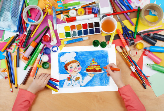 child drawing holiday cake and cook, top view hands with pencil painting picture on paper, artwork workplace